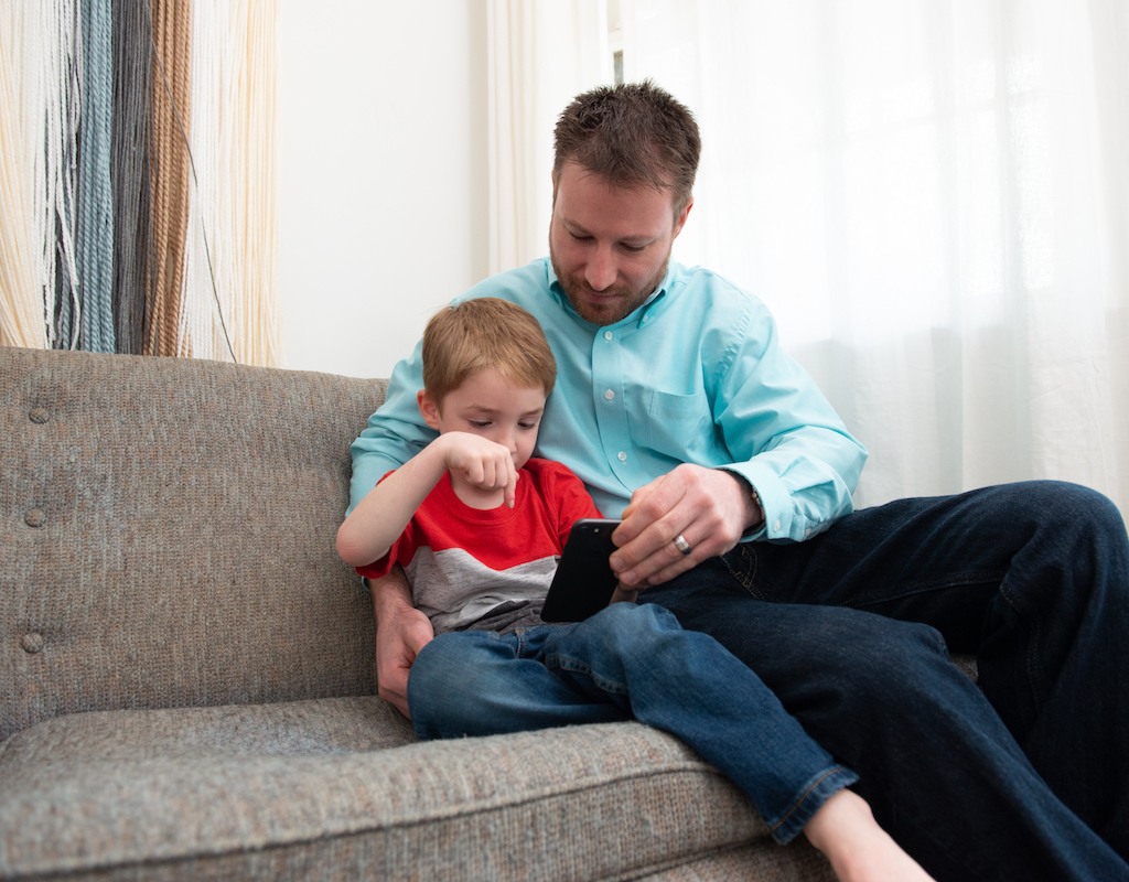 Child with father on couch with phone